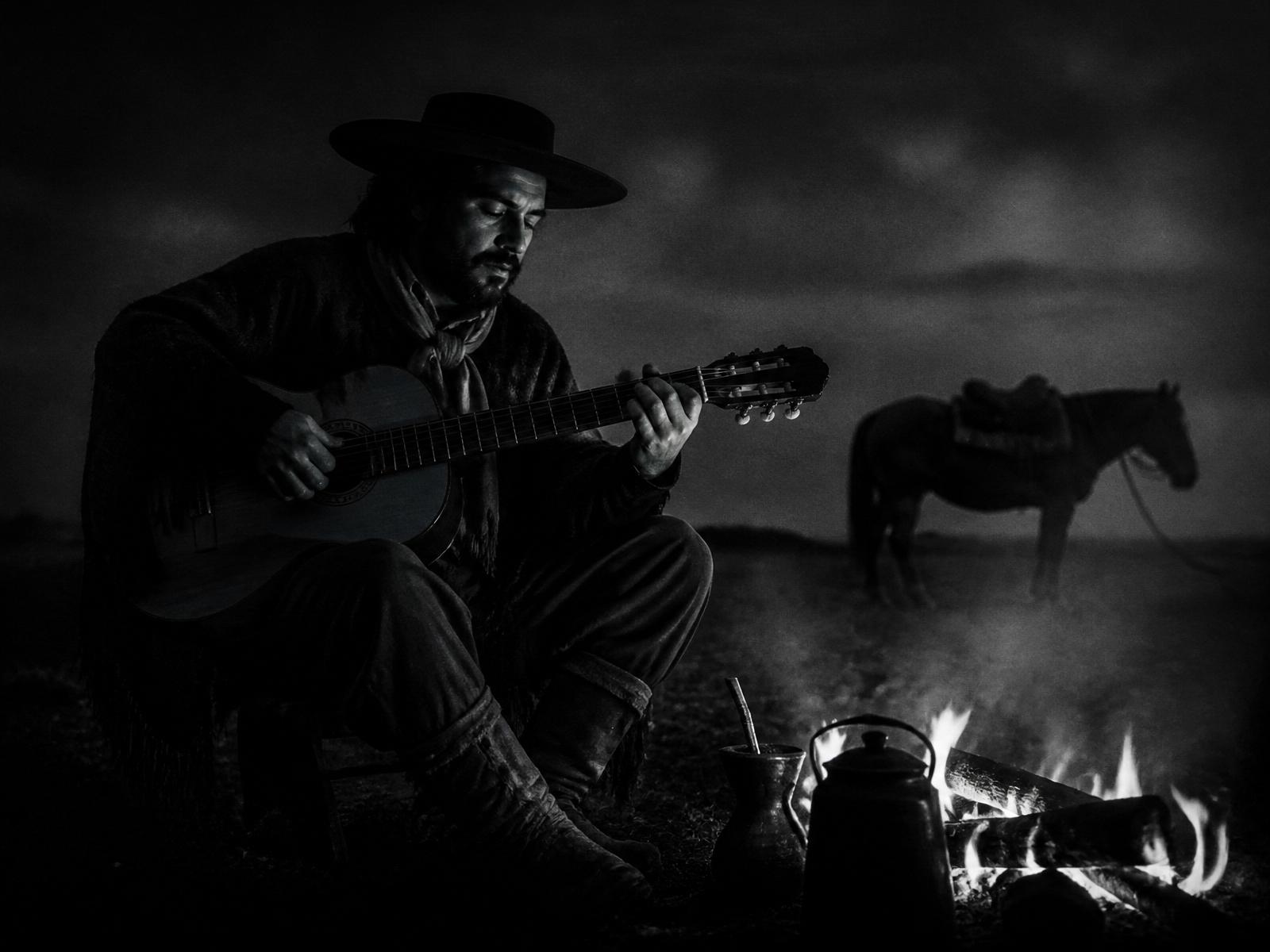 Celino Leite tocando violão ao redor do fogo no pampa gaúcho