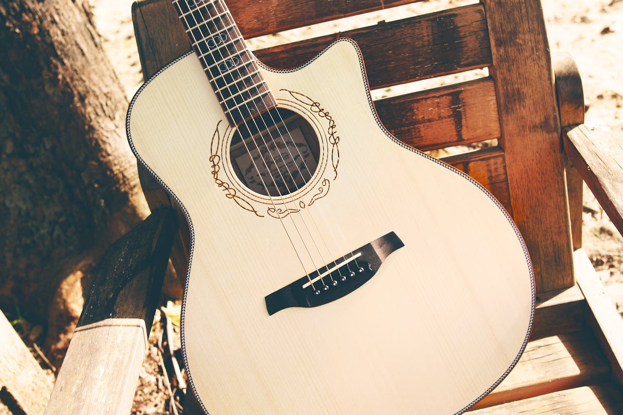 A beautifully crafted vintage acoustic guitar resting on a wooden bench under the sun.
